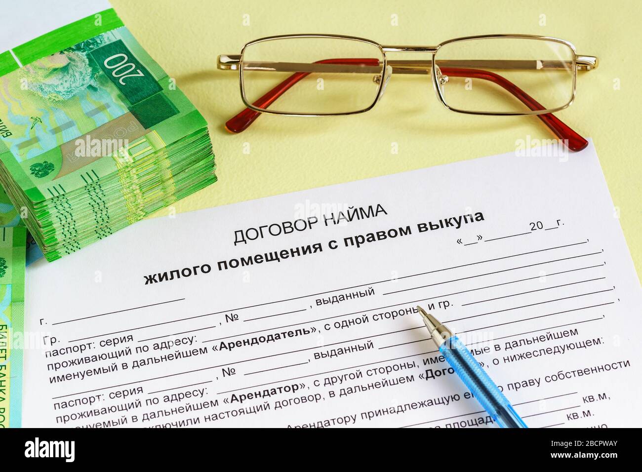 Die Form, den Stift, die Brille und die russischen Rubeln auf dem Tisch. Die Inschrift in russischer Sprache "Vertrag für die Vermietung von Wohnräumen mit dem Recht zu kaufen. Th Stockfoto