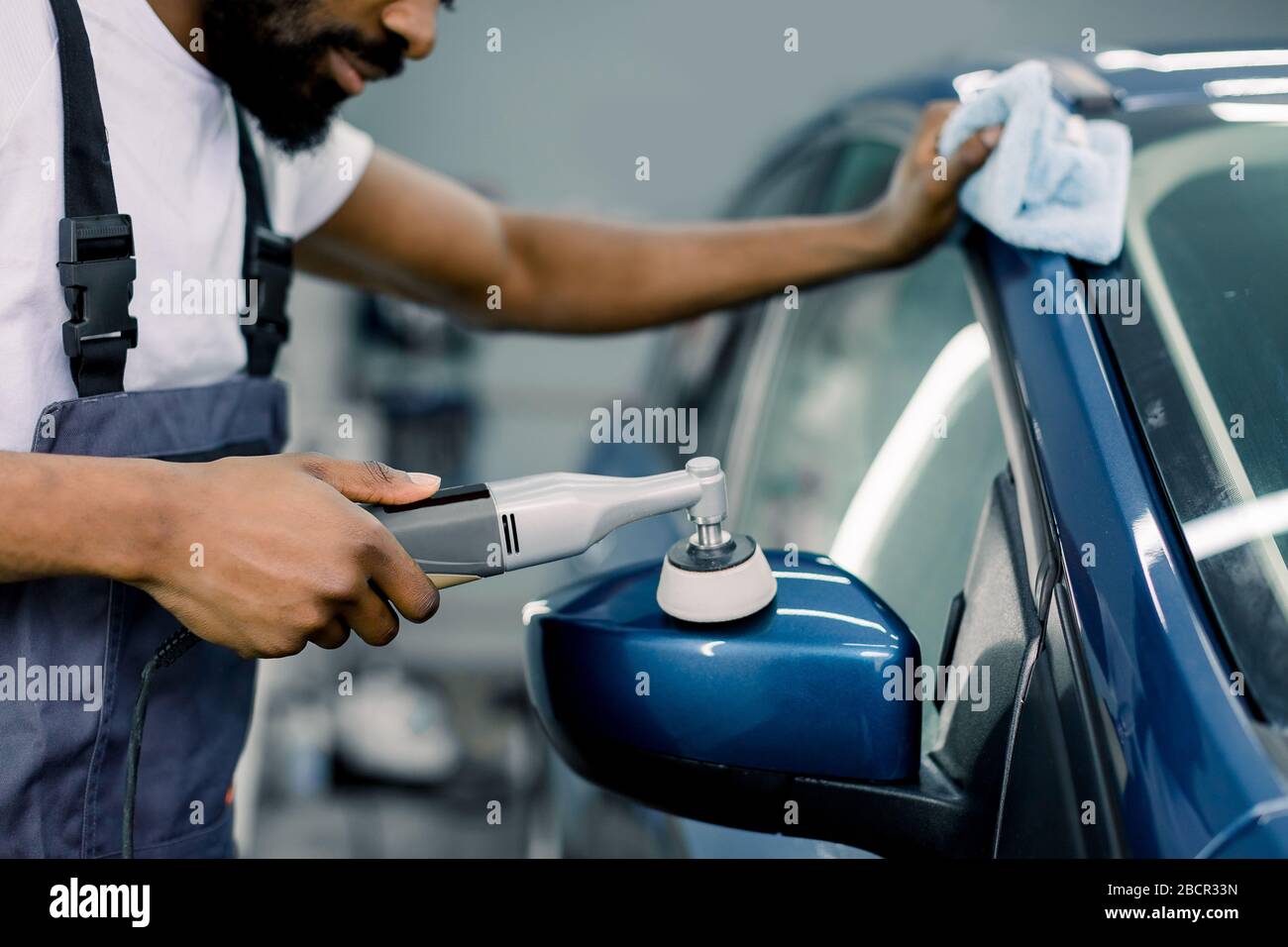 Autodetails und Polierverfahren. Nahaufnahme des jungen afroamerikanischen Mannes, der einen Polierer in der Hand hält und den Autospiegel poliert. Fokus Stockfoto