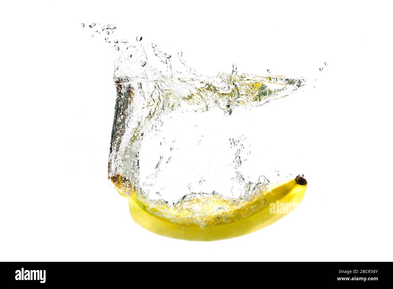 Eine Banane, die auf weißem Grund mit Spritzern in Wasser fällt. Stockfoto