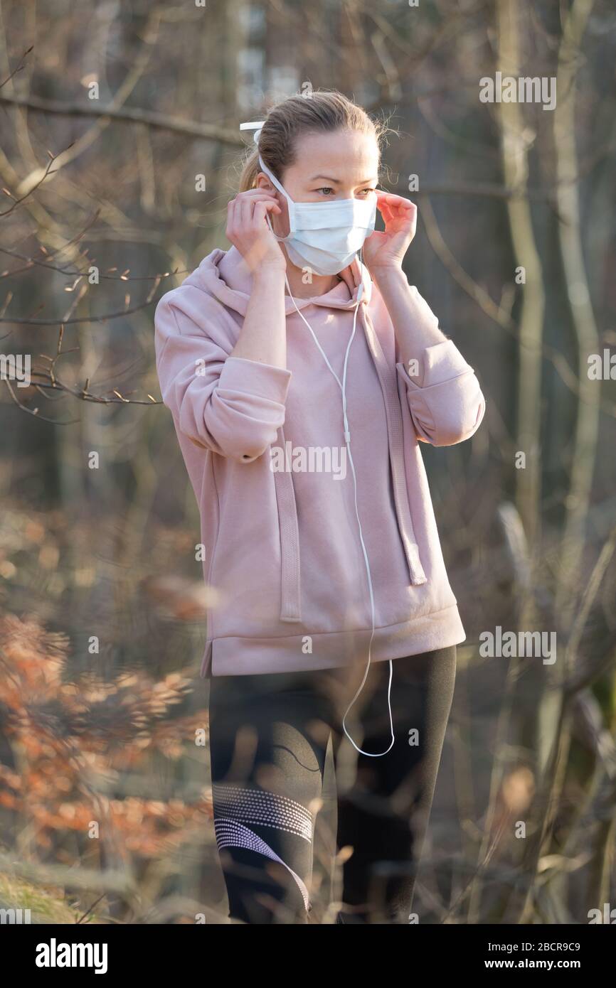 Portrait der kaukasischen Sportfrau, die eine Gesichtsmaske mit medizinischem Schutz trägt, während sie im Park spazieren geht, sich entspannt und Musik hört. Corona-Virus oder Covid Stockfoto