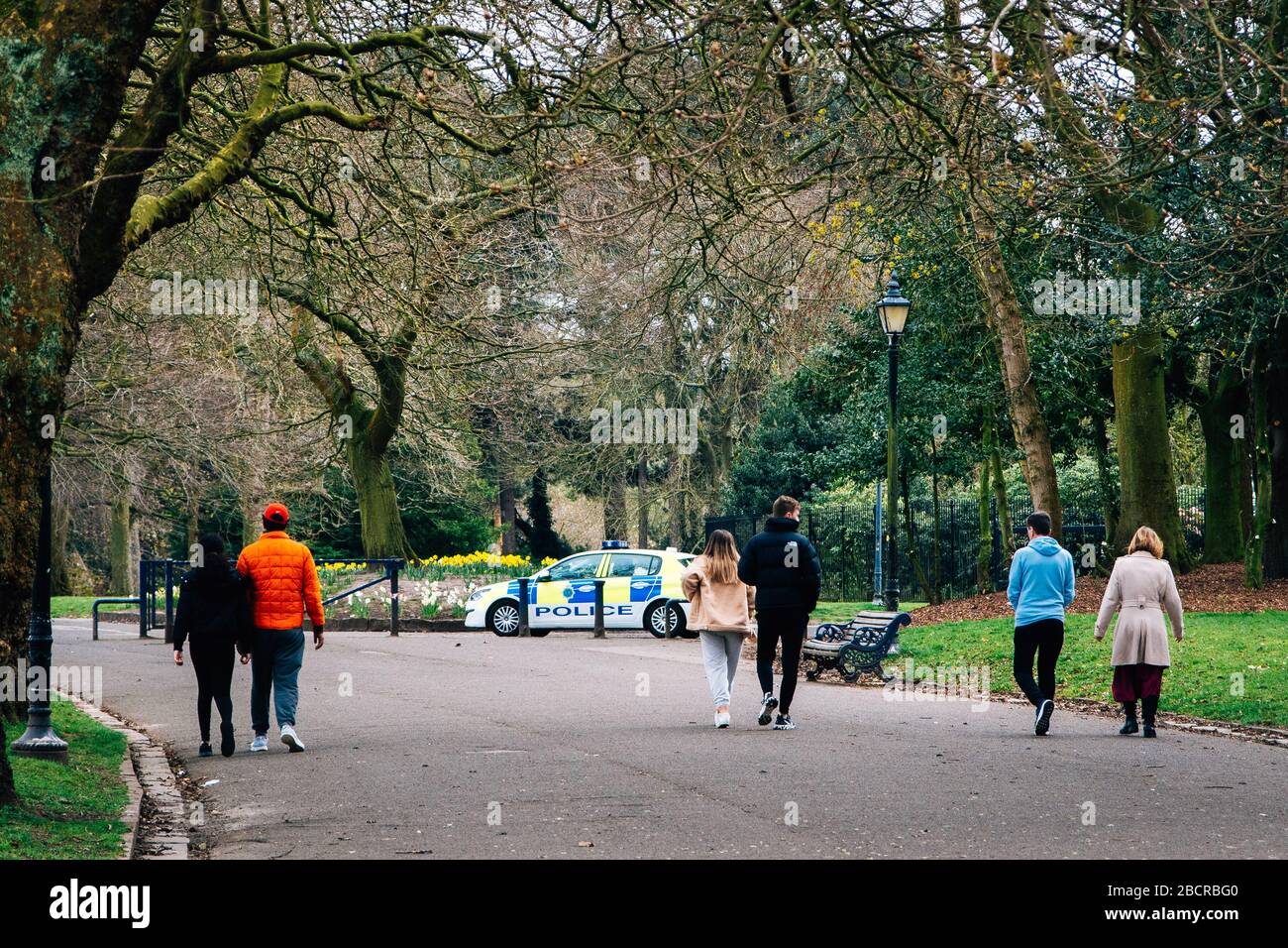 Soziale Distanzierung Großbritannien. Menschen draußen genießen einen Spaziergang in Liverpools Sefton Park während der Coronavirus-Sperre. Polizeiauto im Hintergrund patrouilliert Stockfoto