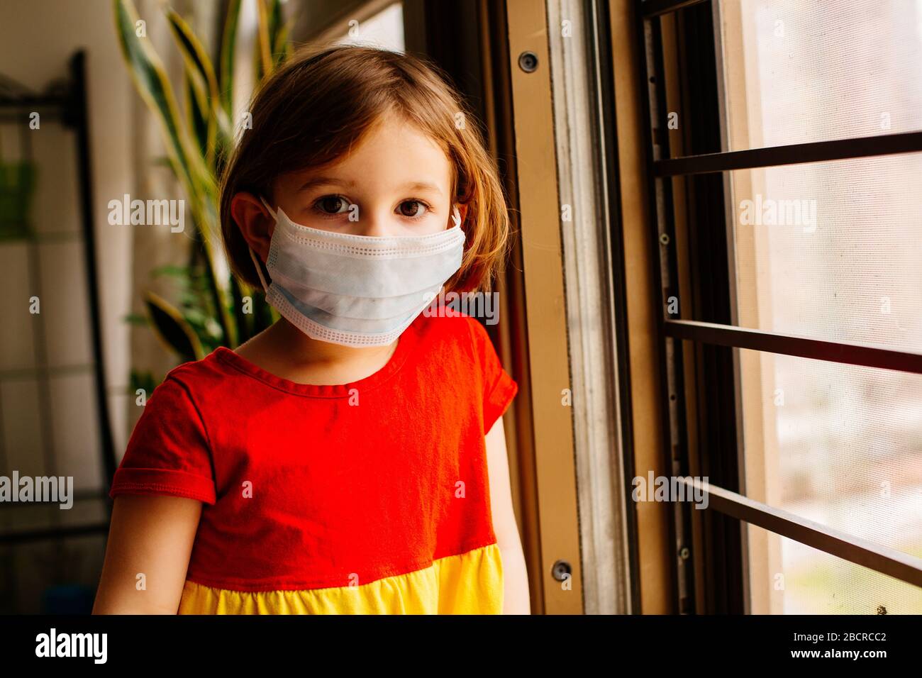 Portrait eines Kleinkindes mit Virusschutz chirurgische Gesichtsmaske, die wegen Coronavirus zu Hause bleibt, um soziale Distanzierungen zu erreichen Stockfoto
