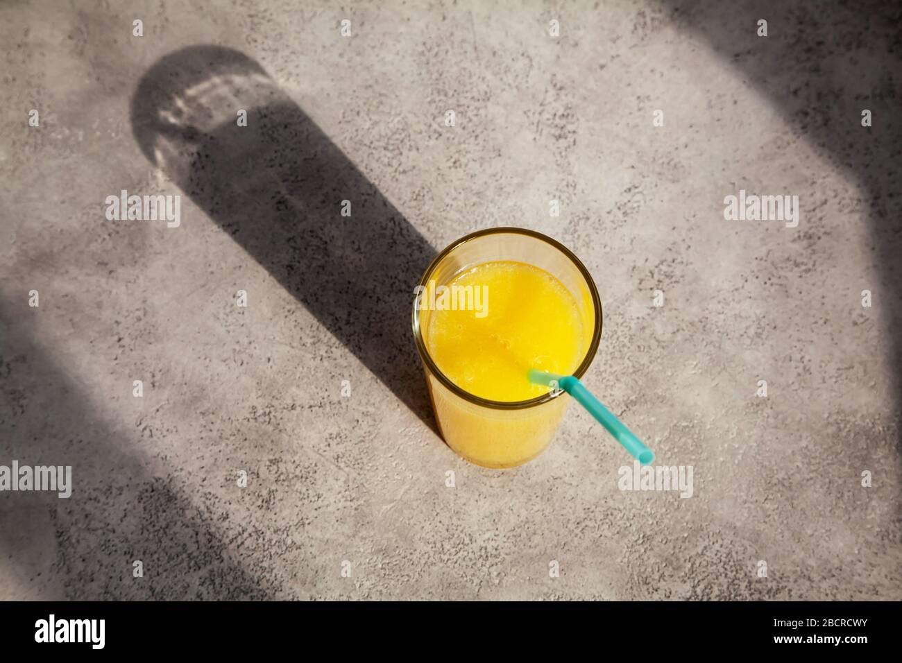 Ein Glas frischen organischen Orangensafts auf grauem Betongrund. Trinken Sie in der Sonne mit einem schönen Schatten Stockfoto