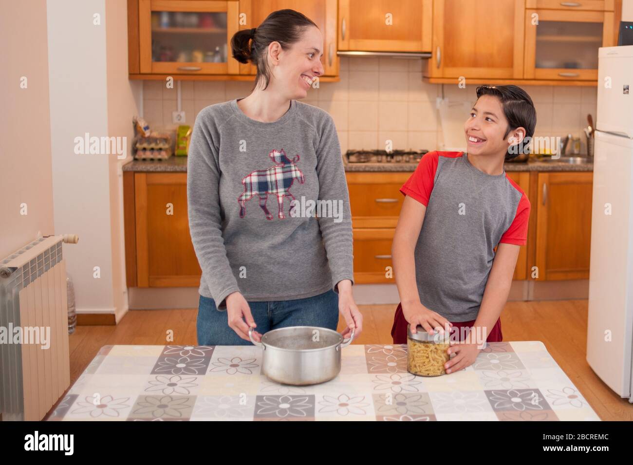 Mutter und Sohn kochen Pasta zusammen. Er öffnet die Flasche und die Mutter hält die Pfanne. Stockfoto