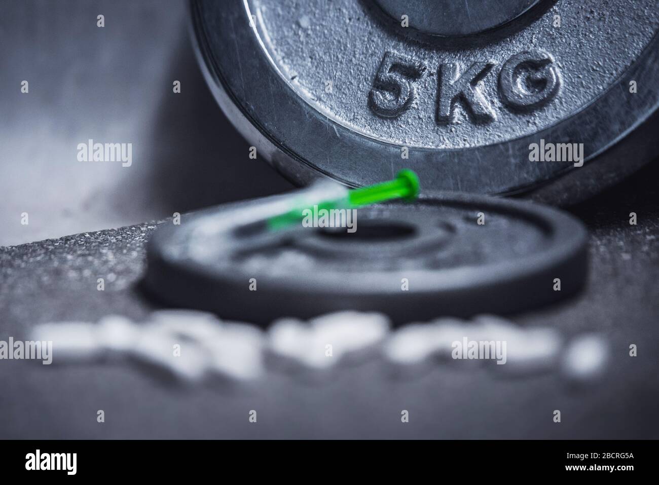 Eine Flasche Dopingmittel und Spritze werden in der Sporthalle auf den schwarzen Boden gelegt Stockfoto