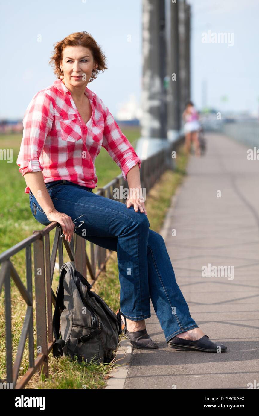 Reife kaukasische Frau mit Rucksack, der auf der Straße der Stadt sitzt, ruhender Wanderer Stockfoto