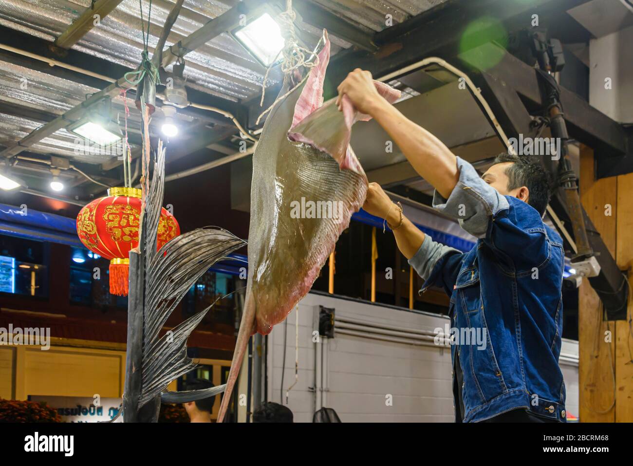 Ein Koch schneidet ein großes Steak von einem Strahlenfisch, während es in der Küche eines Restaurants, Phuket, Thailand, hängt Stockfoto