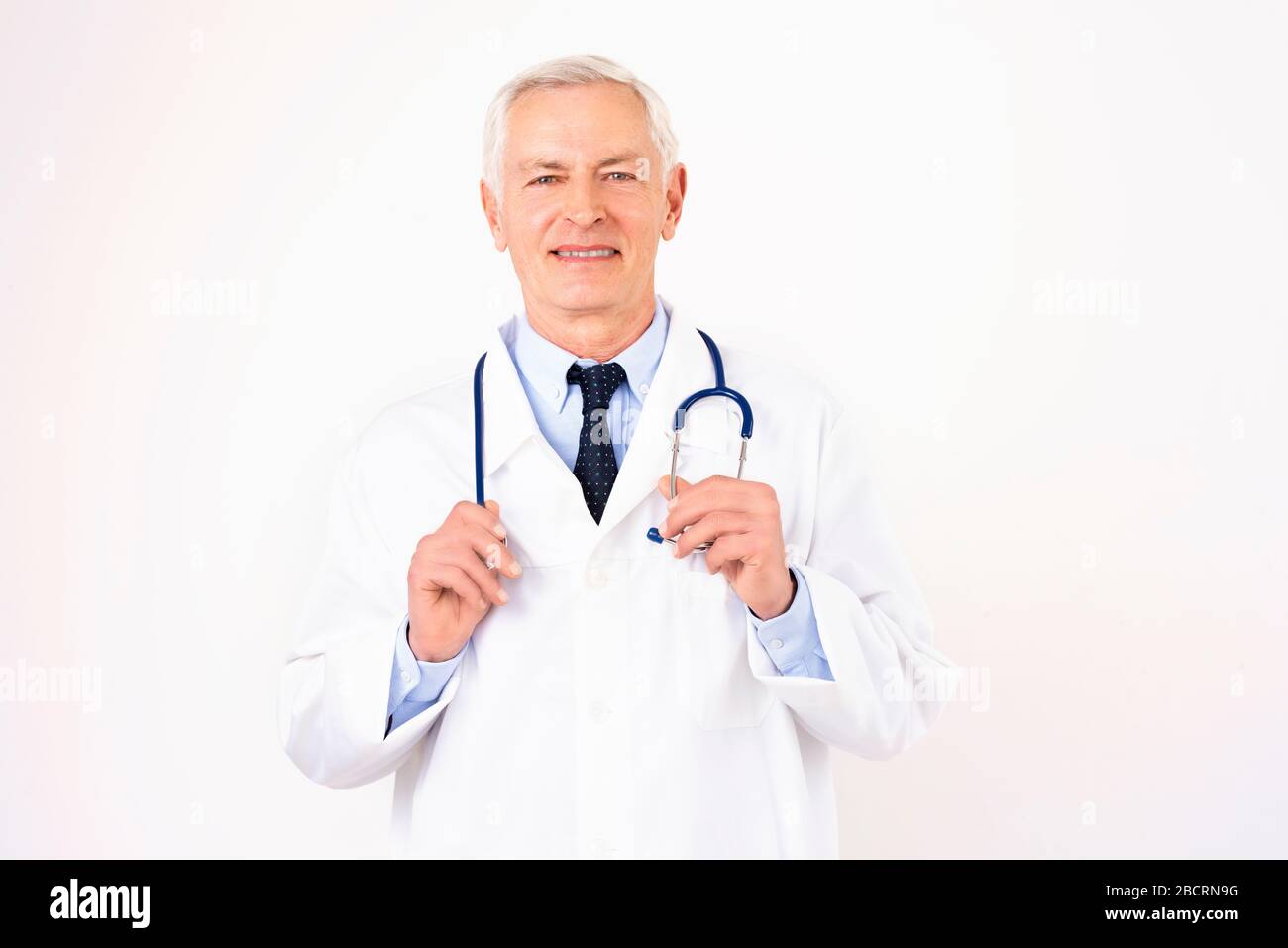 Portraitaufnahme eines männlichen Oberarztes mit Stethoskop um den Hals mit Uniform, während er auf isoliertem weißem Hintergrund steht. Stockfoto