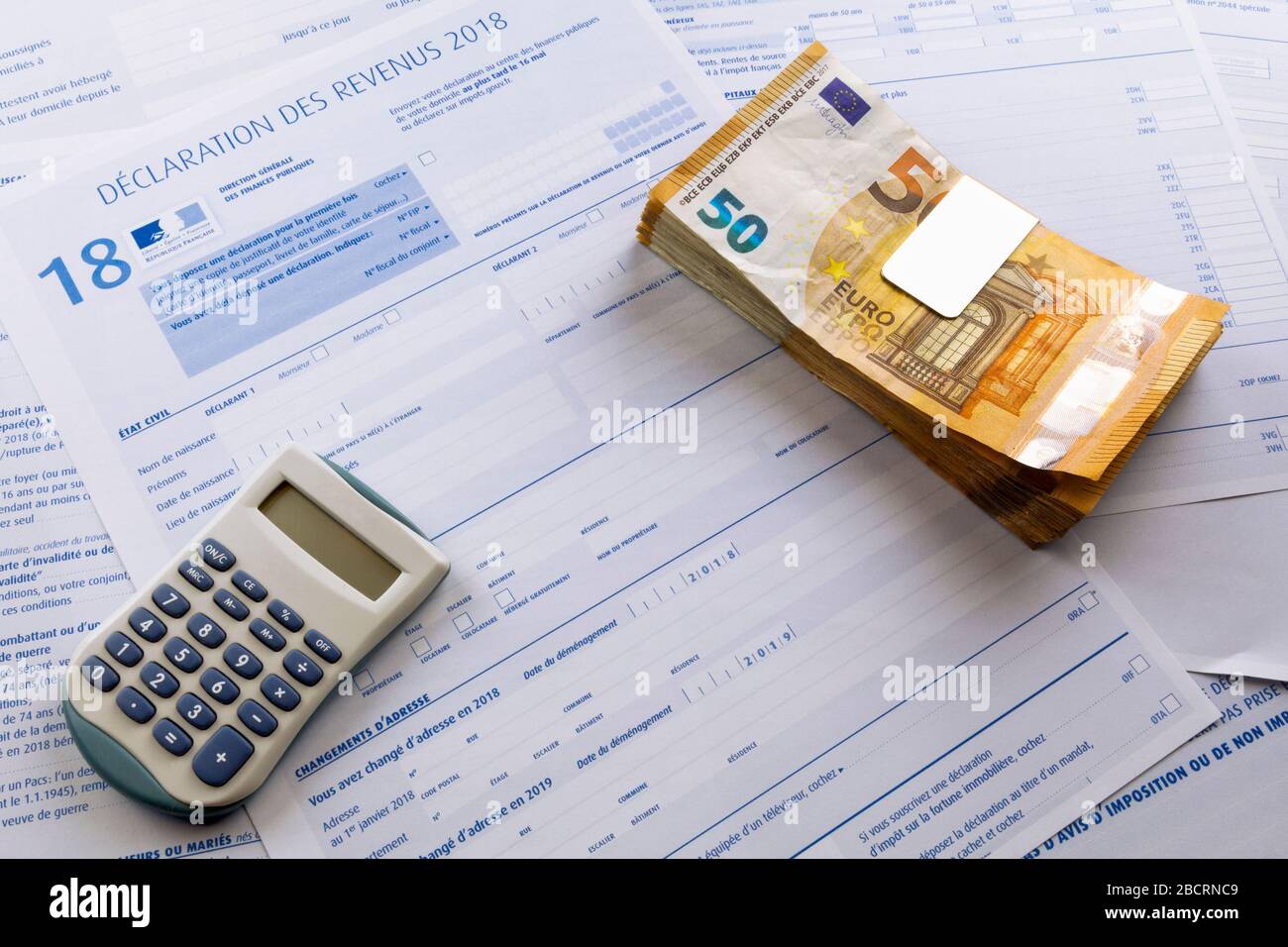 Ein Taschenrechner und ein Stapel von 50 Euro-Banknoten auf der Spitze einer französischen Einkommensteuerform. Stockfoto