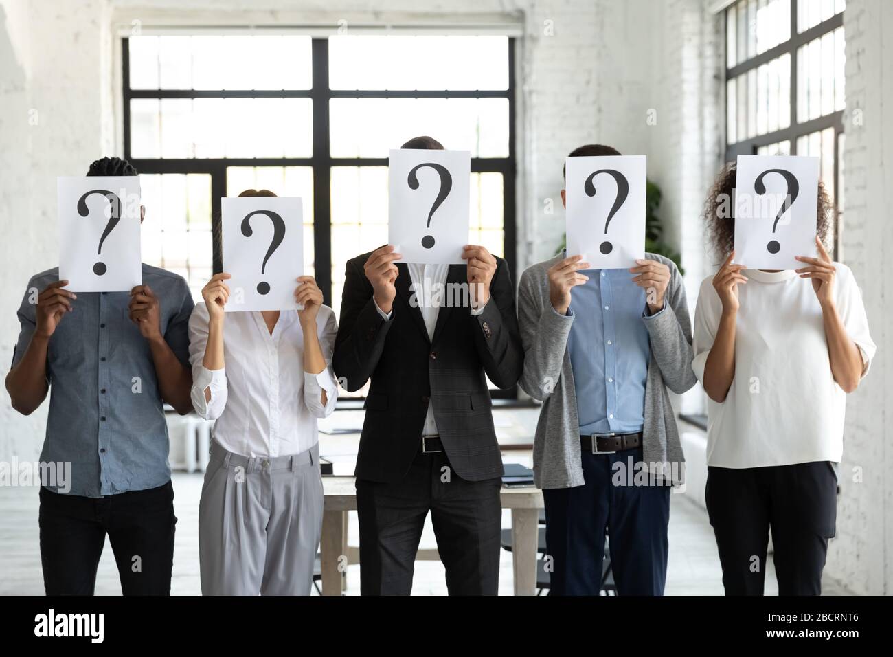 Geschäftsleute verstecken Gesichter hinter Papierblättern mit Fragezeichen. Stockfoto