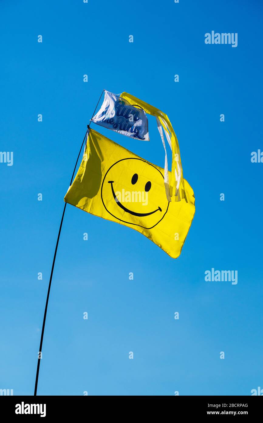 Gelbe Fahne mit Smiley-Symbol auf Teleskop-Anzeigestange, mit Windbock und Markierung "Ring laufen". Alles vor blauem Himmel. Stockfoto