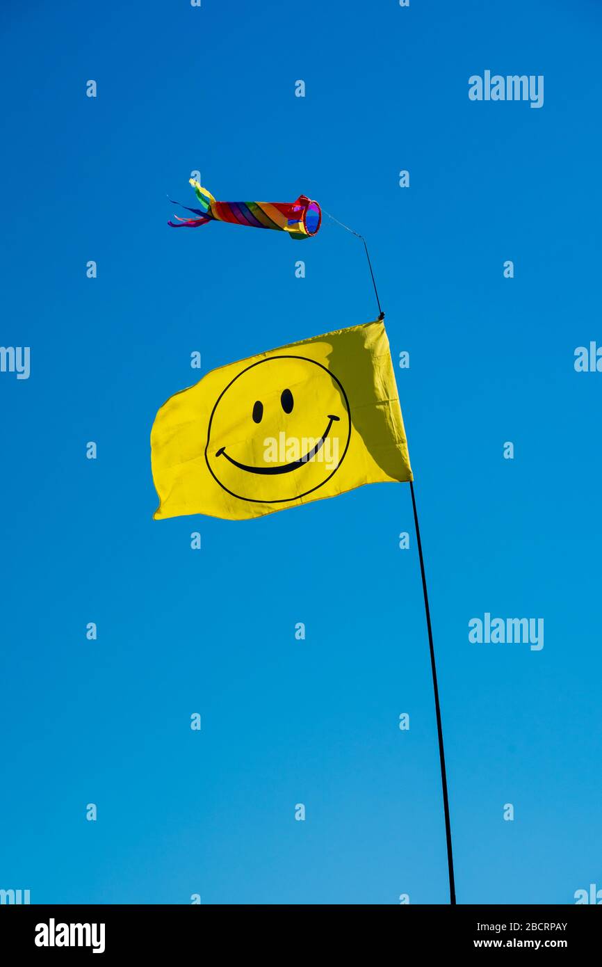 Teleskop-Displaystange mit gelber Smiley-Fahne und buntem Windbock gegen blauen Himmel. Perry Green, Much Hadham, Hertfordshire Stockfoto
