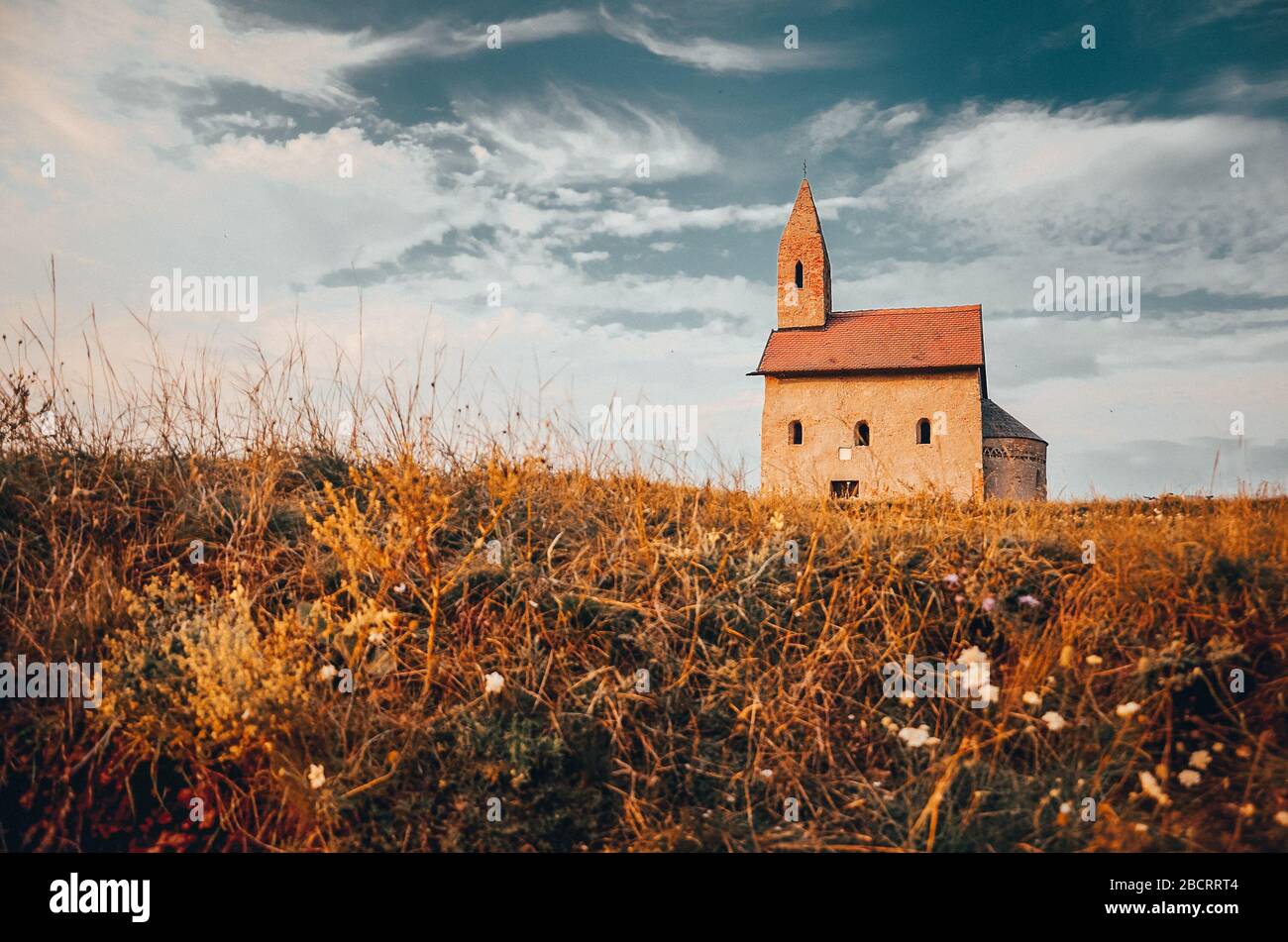 Kleiner Mann auf dem Fahrrad in der Nähe der alten katholischen Kirche in der slowakei auf einem Hügel während des Sommers Sonnenuntergang Stockfoto