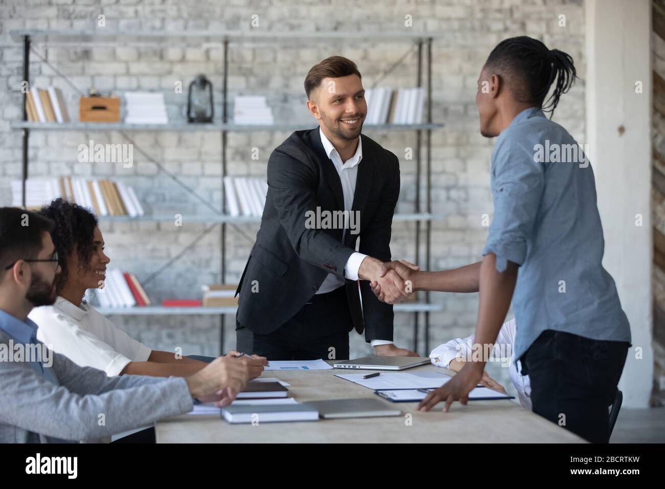 Geschäftsmann im Anzug schüttelt Hand von afroamerikanischem männlichen Partner. Stockfoto