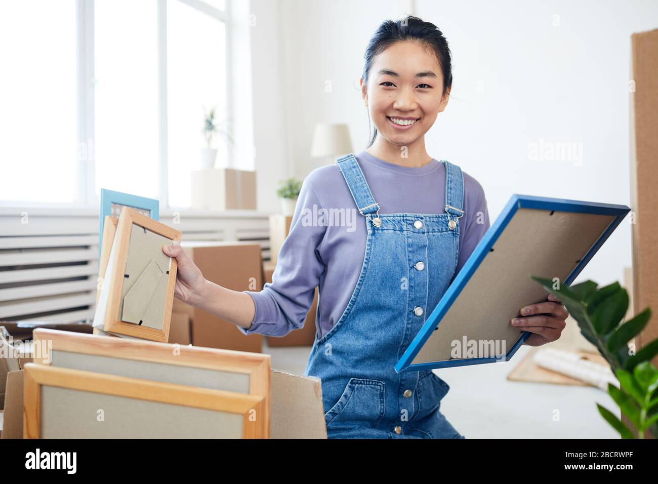 Portrait junger Asiaten, die Boxen packen und mit der Kamera lächeln, freute sich darauf, in ein neues Haus oder eine neue Wohnung zu ziehen, wo sie Platz für Kopien haben Stockfoto