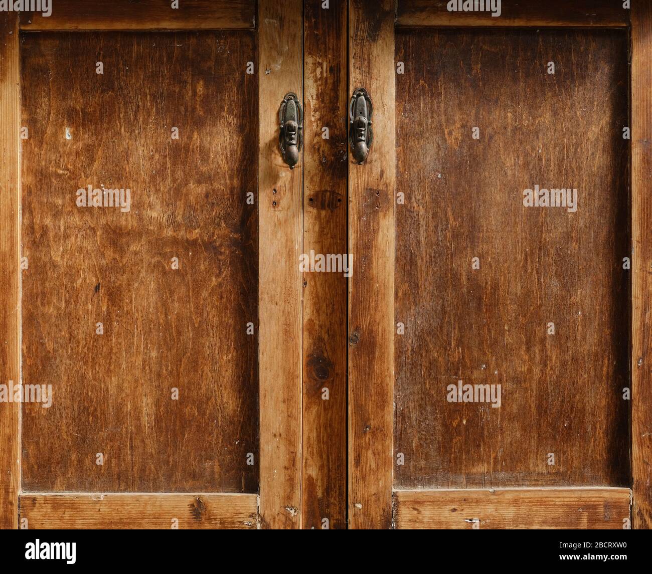 Hochauflösendes Foto von geschlossenen alten Holztüren aus Eiche mit Messinggriffen, aufgenommen in natürlichem Morgenlicht. Stockfoto