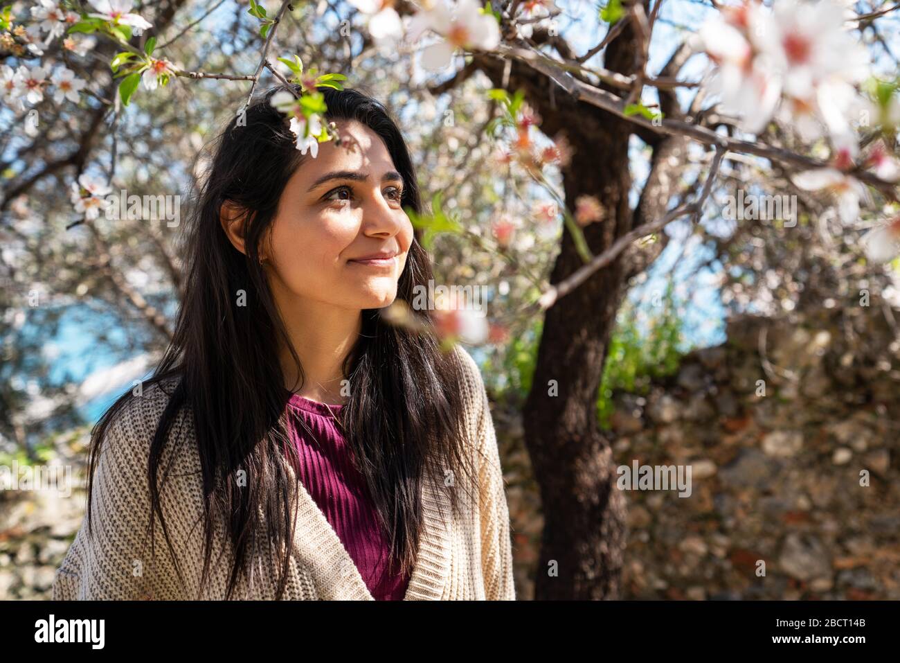 Junge Frau, die den Blick und das Sonnenlicht auf ihrem Gesicht unter Pflaumenbaum mit Blumen genießt Stockfoto