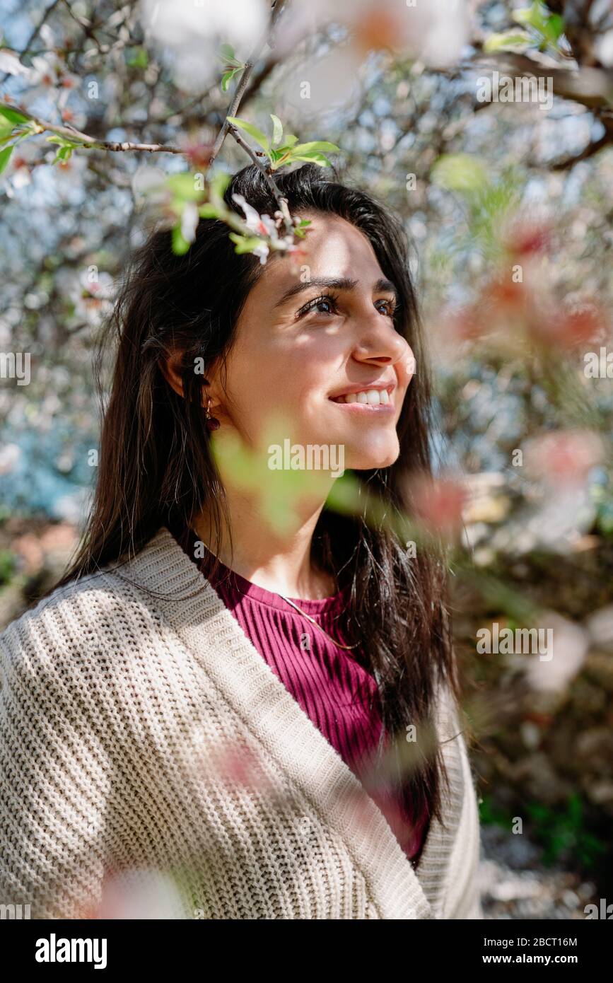 Junge Frau, die den Blick und das Sonnenlicht auf ihrem Gesicht unter Pflaumenbaum mit Blumen genießt Stockfoto