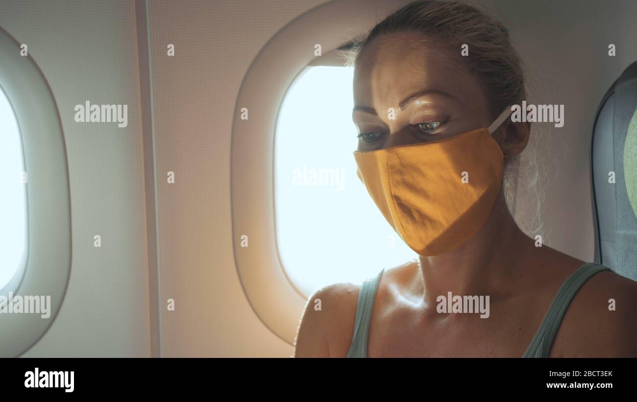 Frau reist kaukasisch im Flugzeug mit einer schützenden medizinischen Maske. Mädchen Tourist im Flugzeug mit Schutzmaske. Coronavirus Kovid 19. Stockfoto