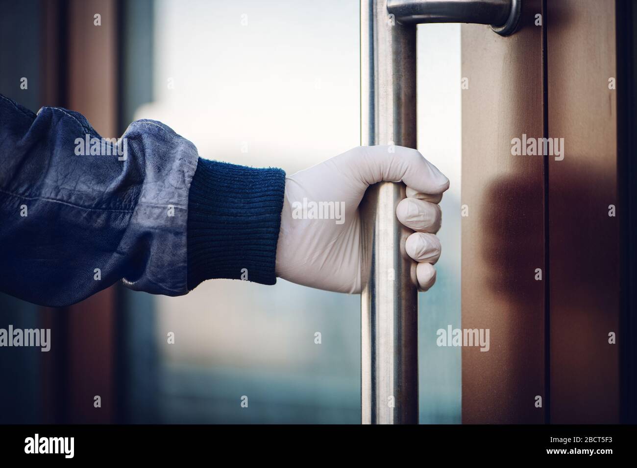 Die männliche Hand in weißem Latexhandschuh hält den Griff beim Öffnen der Tür. COVID-19 Pandemie-Konzept. Stockfoto