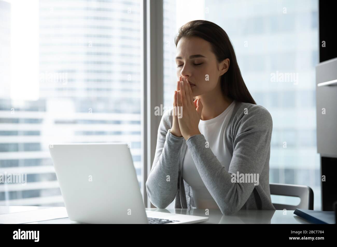 Religiöse weibliche Angestellte, die am Arbeitsplatz zu gott beten Stockfoto