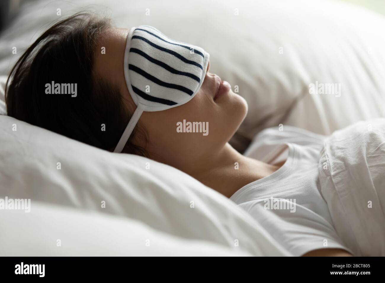 Junge Frau in Schlafmaske, die sich im bequemen Bett entspannen kann Stockfoto