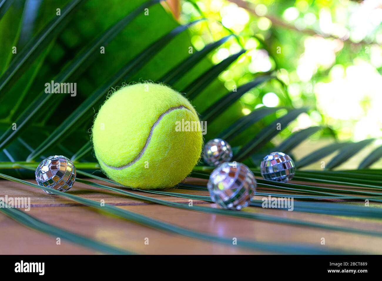 Tennislayout mit Tennisball und Disco-Bällen auf tropischem Palmblatt-Hintergrund. Sportparty-Konzept. Flache Lage, Draufsicht, selektiver Fokus. Stockfoto