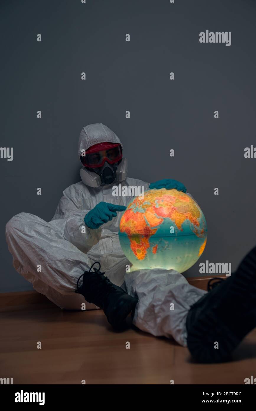 Konzept: Weltweite Viruskrise. Frau im Laborkittel, Nitrilhandschuhe, Brille, Gesichtsmaske und NBC-Anzug für Covid-19 Coronavirus, auf dem Boden von ihr sitzend Stockfoto