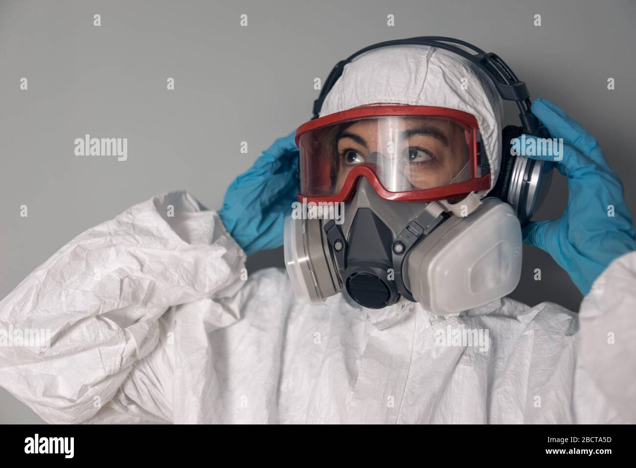 Frau mit Laborkittel, Nitrilhandschuhen, Schutzbrille, Gesichtsmaske und NBC-Schutzanzug, Musik mit Kopfhörern hören. Stockfoto