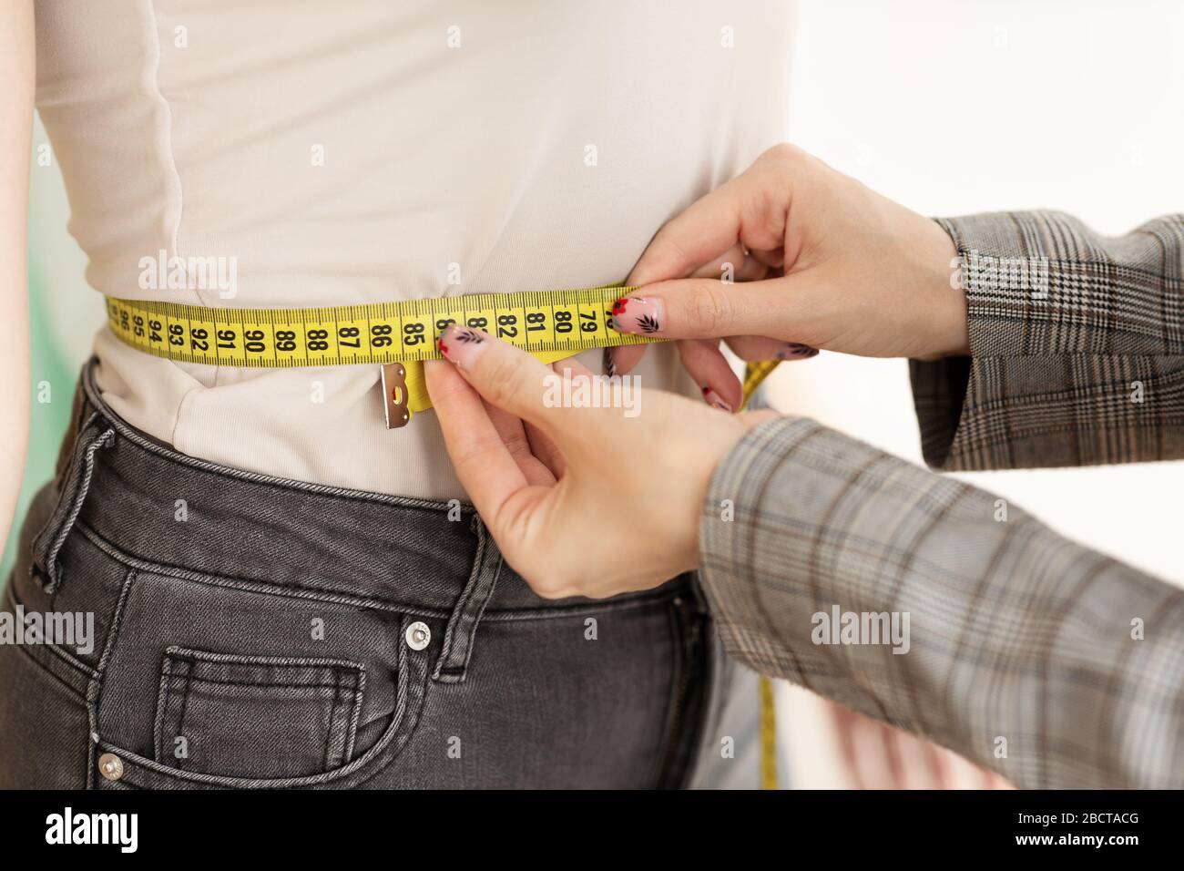 Die Hände des weiblichen Designers messen die Taille der jungen Frau Stockfoto