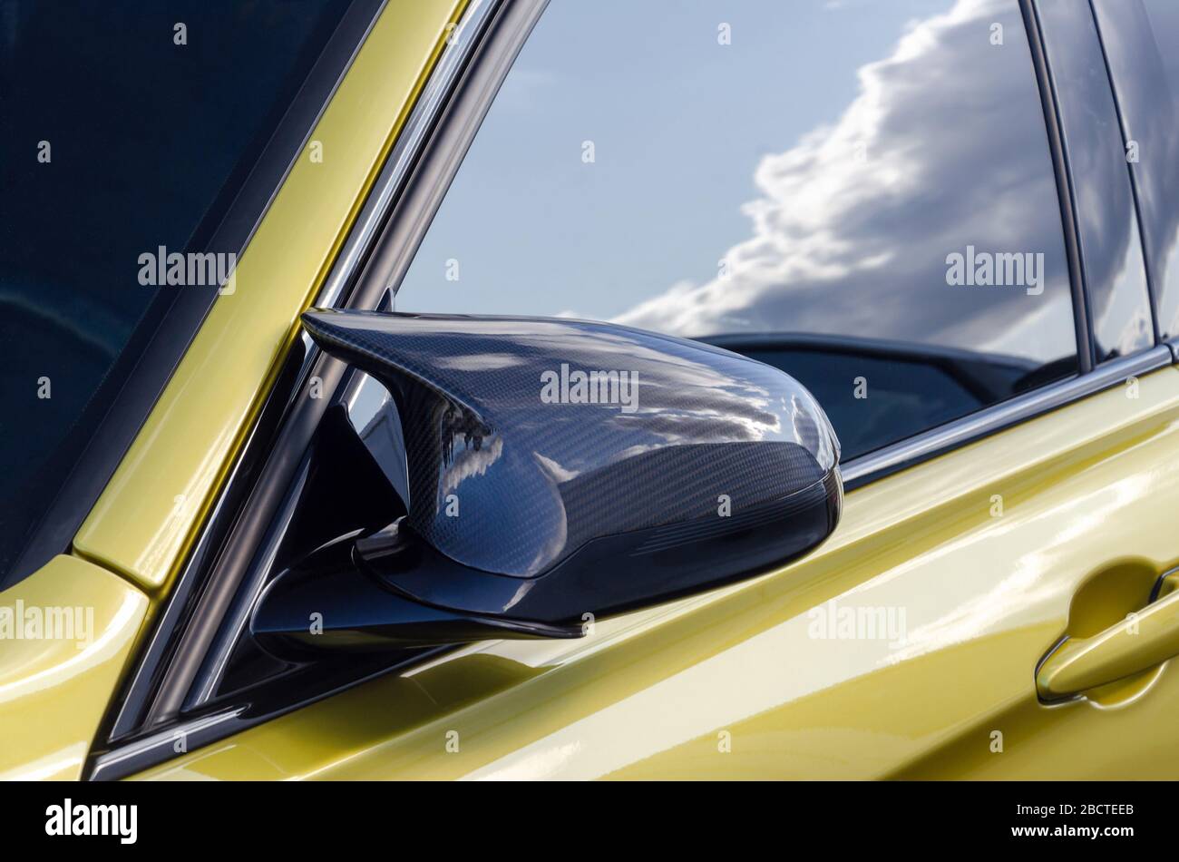 Teil eines teuren Sportwagens. Carbon-Spiegel. goldene Farbe Auto. Auf der Tür Fenster die Reflexion des Himmels Stockfoto