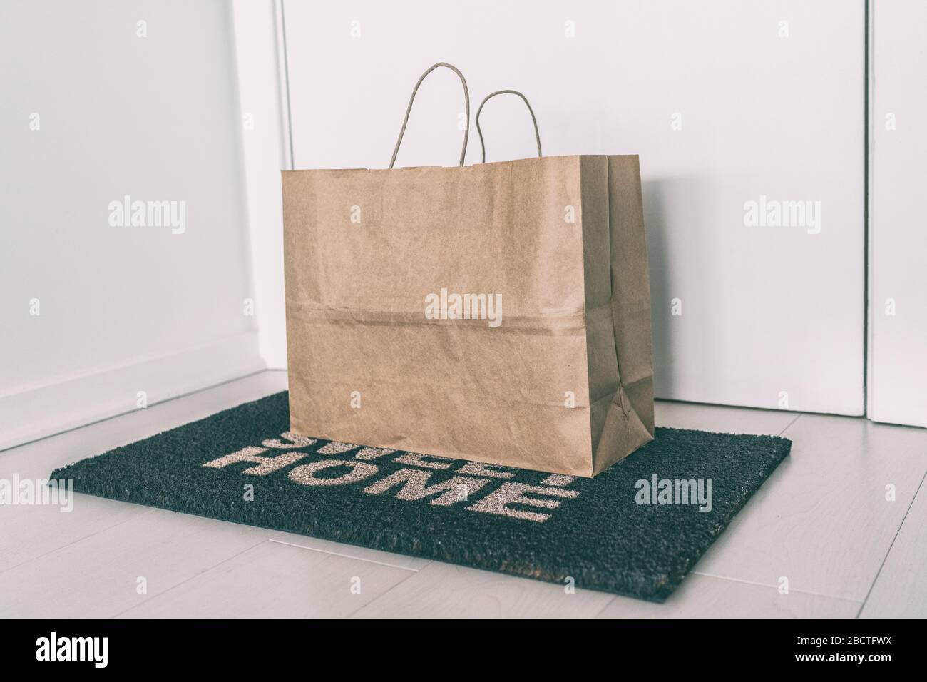 Hauslieferung von Lebensmitteltüten an der Türmatte für Corona-Viren, die Sicherheit verbreiten. Vorsichtsmaßnahmen gegen COVID-19, ohne Kontakt ausgelieferte Papiertüte. Stockfoto