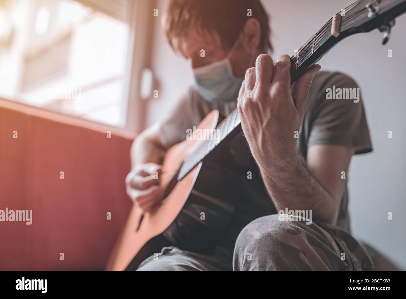 Mann, der zu Hause akustische Gitarre spielt, Quarantäne sich während des Covid-19-Coronavirus-Ausbruchs Stockfoto