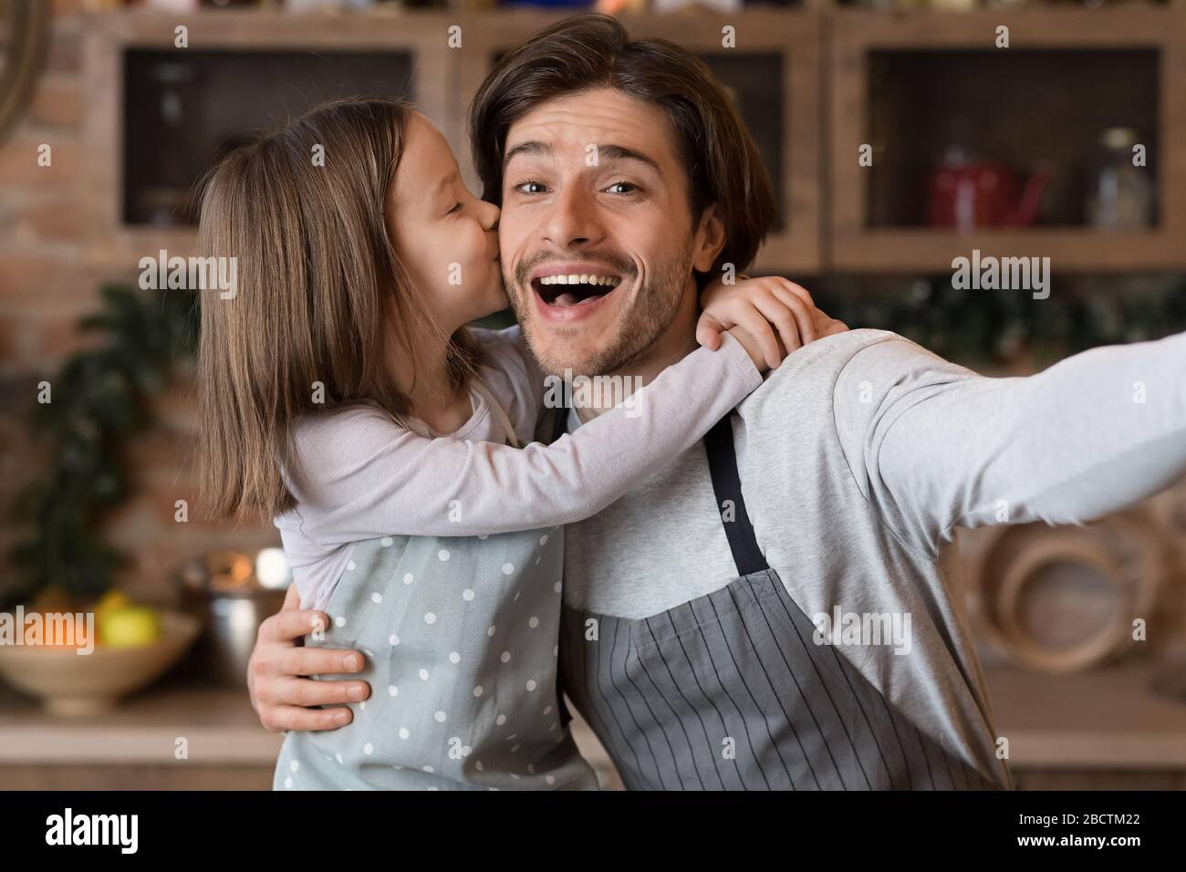 Kleines Mädchen, Das Vater Küsst, Während Sie Selfie In Kitchen Nehmen Stockfoto