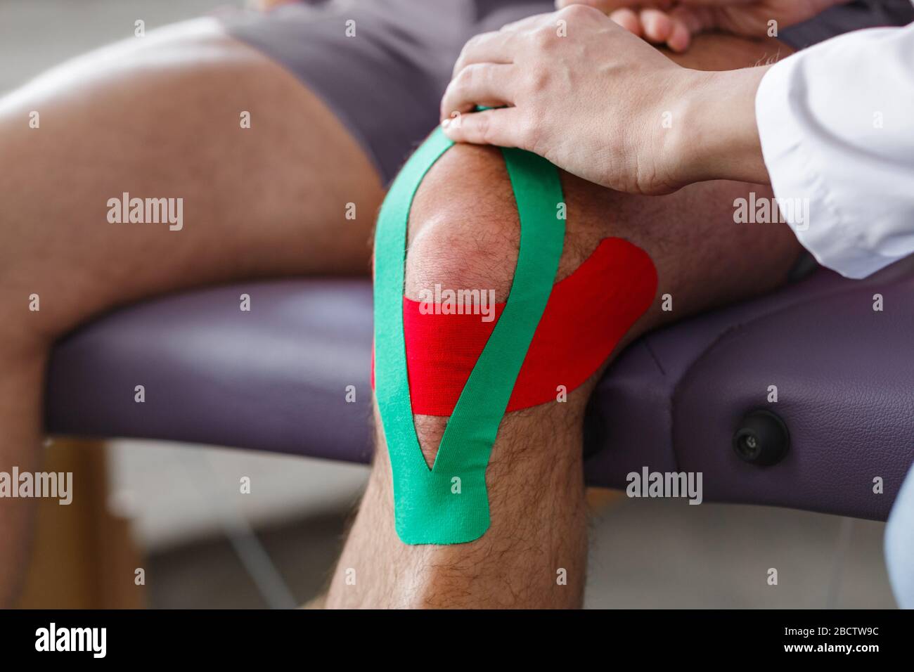 Kinesiologie Taping.Physikalischer Therapeut Anwendung von Kinesiologieband auf den Patienten Knie.Therapeut Behandlung verletzter Knie des jungen Athleten.Post traumatisch Stockfoto