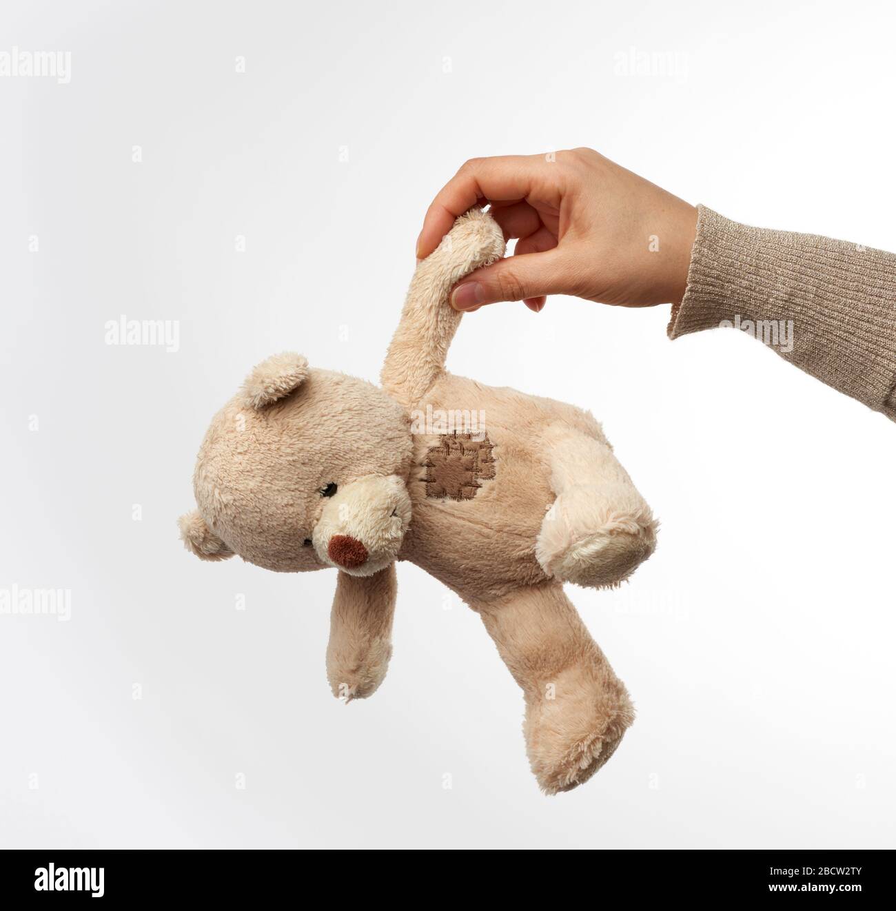 Weibliche Hand hält kleinen beige niedlichen Teddybären mit Flecken, Spielzeug auf weißem Hintergrund Stockfoto