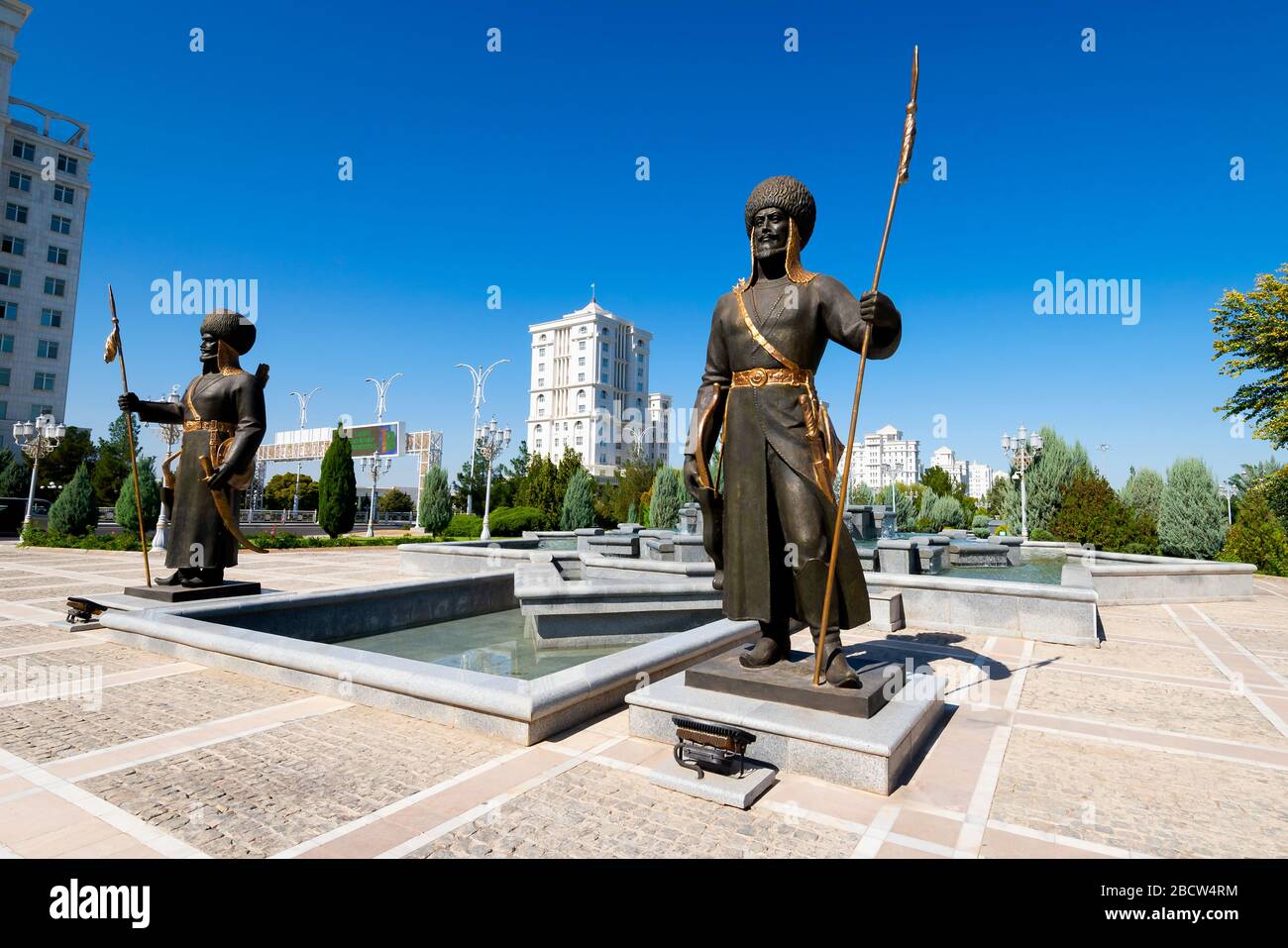 Statue von Soldaten in Bronze im Independence Park in Ashgabat, Turkmenistan. Weiße Marmorgebäude sichtbar hinter Skulpturen und Wasserbrunnen. Stockfoto