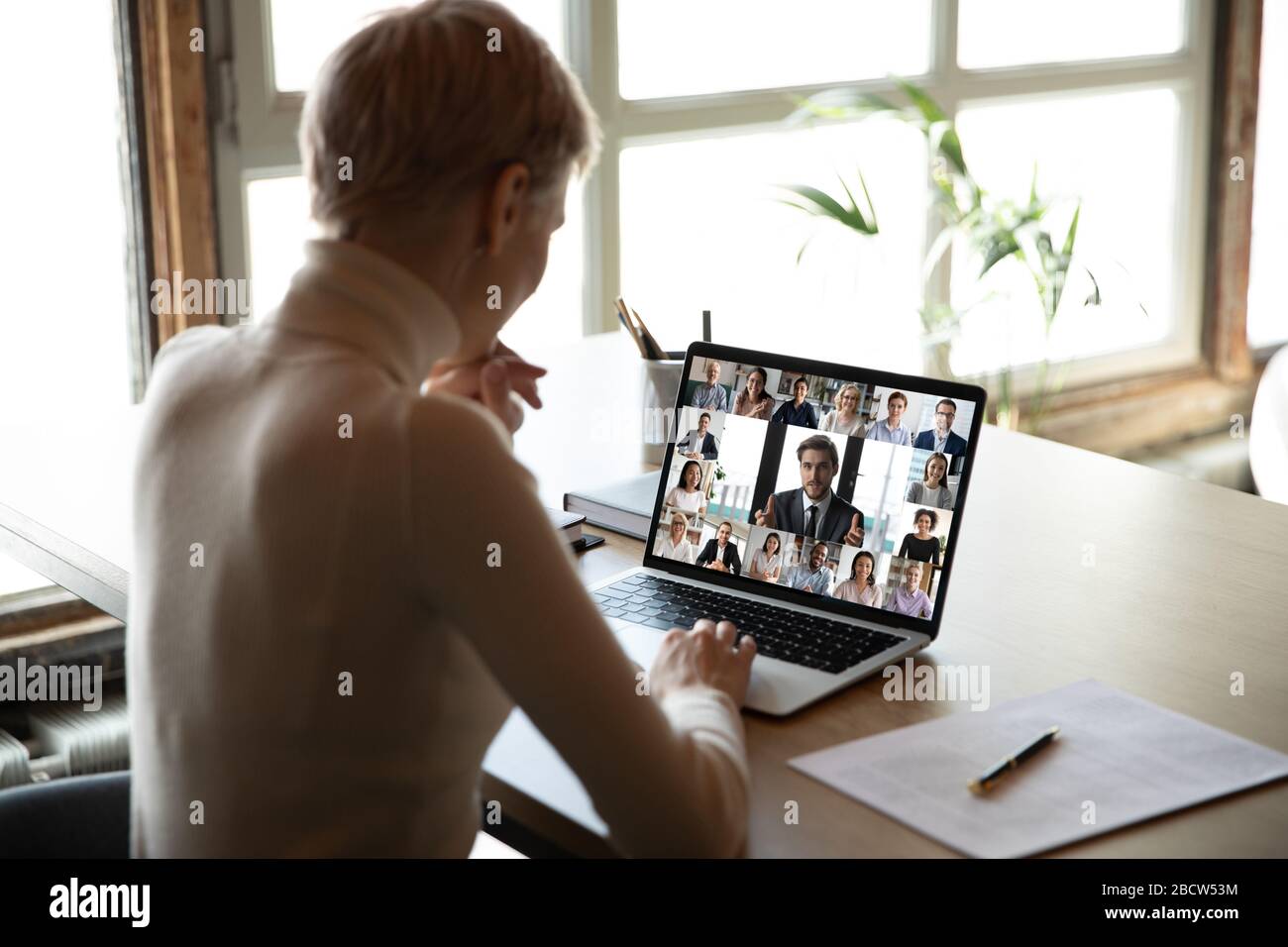 Frau sitzt am Schreibtisch und sieht sich die neue Videokonferenzanwendung online an Stockfoto