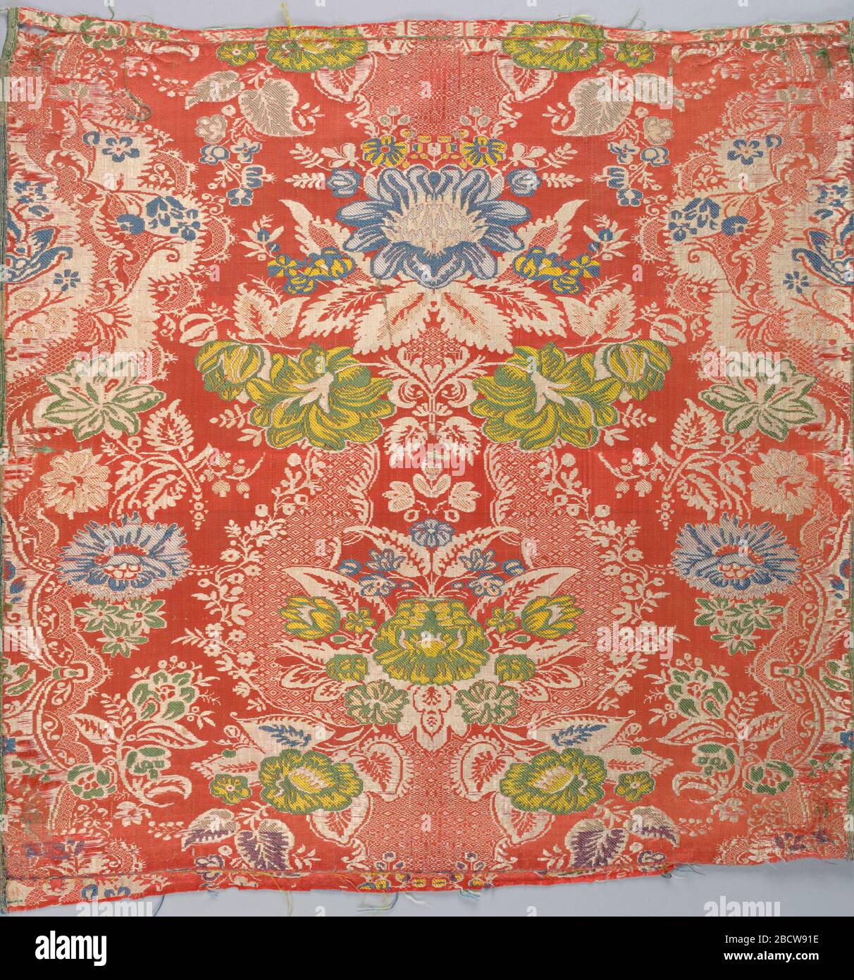 Fragment. Forschung im Bereich ProgressFragment von broierter Seide mit weißem symmetrischem Blumen- und spitzenarmiger Muster auf orangefarbenem Boden. Zusätzlicher Schwimmer aus Gelb, Grün, Blau und Creme. Breite Auswahl, Warp-schnurgebunden und gestreift. Fragment Stockfoto