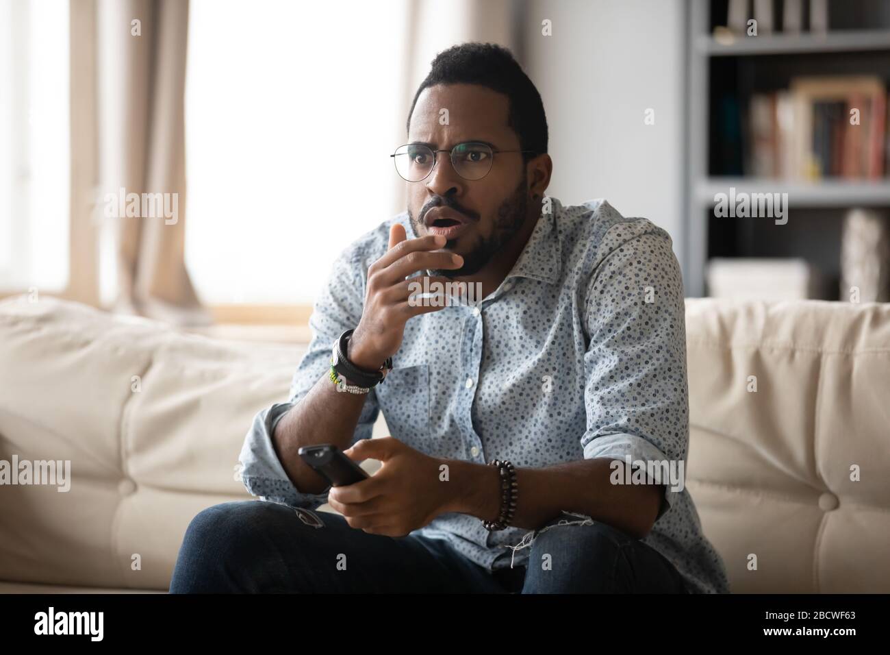 Ängstlicher afroamerikanischer Mann, der zu Hause Fernsehen sieht Stockfoto