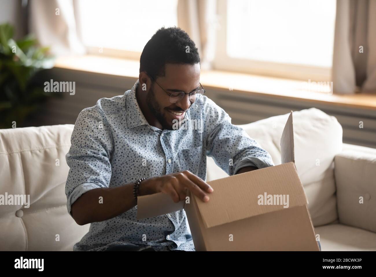 Aufgeregter birazialer Mann entpackt das Paket für die Internetlieferung Stockfoto