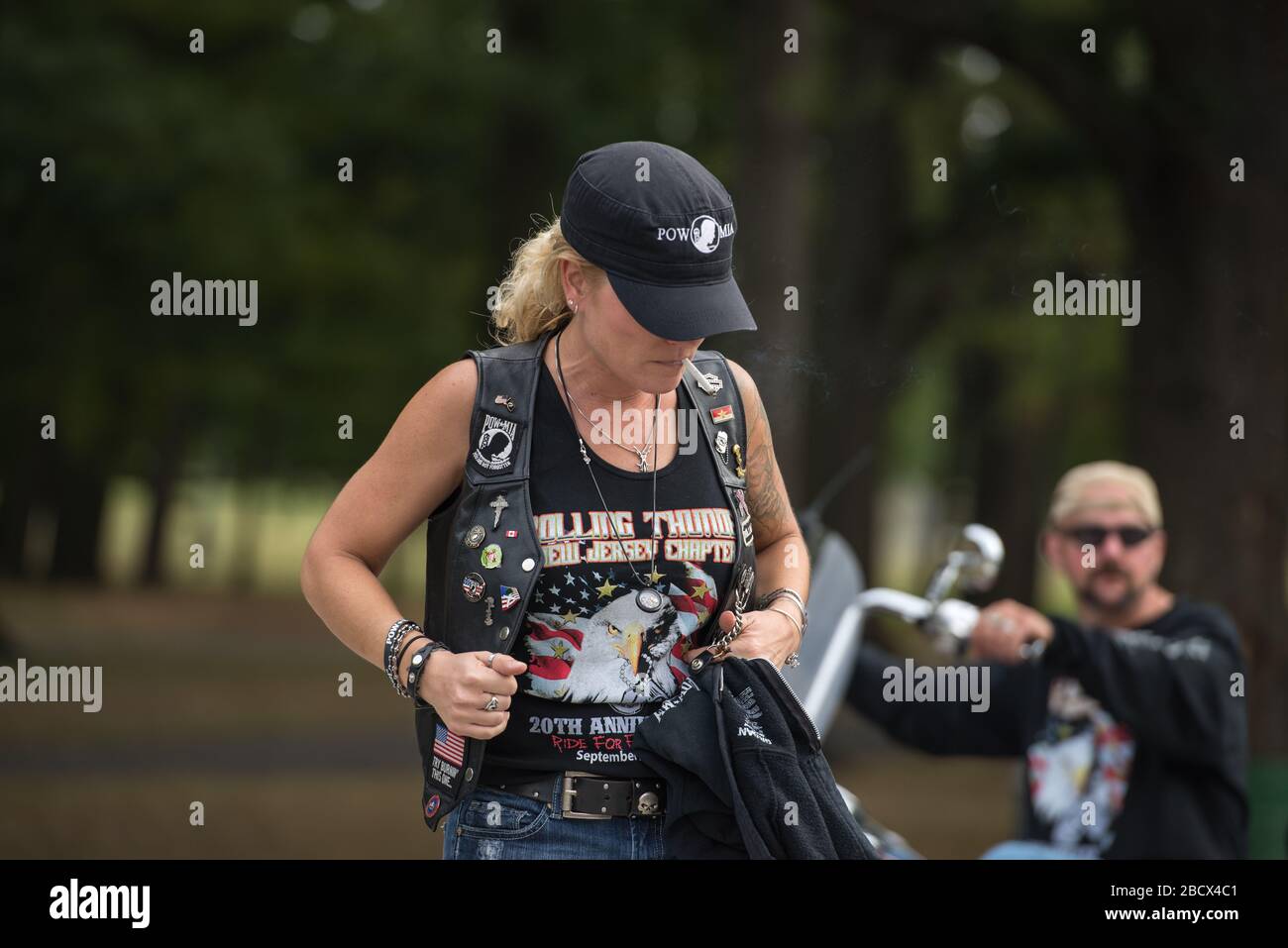 Eine kaukasische, blonde Frau bei einem Rolling Thunder Event, die eine schwarze Mütze und schwarze Kleidung mit Kriegsemblemen trägt. Ein Biker ist im Hintergrund. Stockfoto