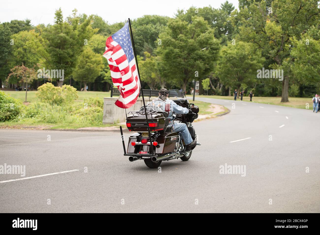 Rolling Thunder Motorradfahrer, der mit einer großen amerikanischen Flagge auf der Rückseite seines Fahrrads bei einer Rallye in einem Park in New Jersey wegfährt. Stockfoto