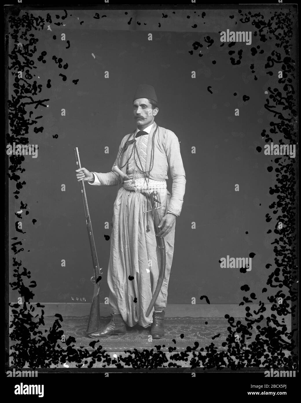 Fares A Ferzan modelt syrisches Kostüm mit Schwert-Dolch und Gewehr. Fares A. Ferzan, vom Libanon, Syrien, war ein Ladenbesitzer in Atlantic City, der in den 1880er Jahren zu mehreren Ausstellungen reiste, wo er feine Seidenwebertechniken demonstrierte. MNH-4069 Stockfoto