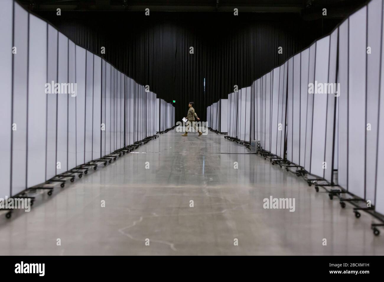 Ein Soldat läuft am 5. April 2020 am Field Hospital im CenturyLink Field Event Center in Seattle an Trennwänden vorbei, in denen sich Reihen von Krankenhausbetten verstecken. Das mobile chirurgische Krankenhaus der Armee, das derzeit für nicht-COVID-19-Fälle vorgesehen ist, umfasst medizinisches Militärpersonal aus mehreren Einheiten, darunter die Soldaten des 10th Field Hospital Hospital Hospital Hospital Hospital des 627. Krankenhauses in Fort Carson, Colorado, die 62. Medizinische Brigade der Joint Base Lewis-Mc-Chord, Washington und andere. Beamte sagten, dass das Krankenhaus jetzt bereit sei, Patienten aufzunehmen. Stockfoto