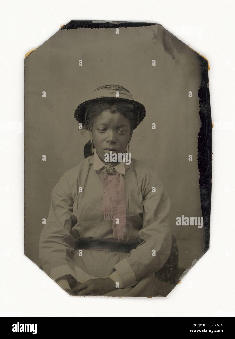 Tintype einer Frau. Eine Weißart einer nicht identifizierten afroamerikanischen Frau in einem Hut, Ohrringen und Kleid. Ihre Wangen sind pink gestrichen, ebenso die vordere Mitte ihres Kleides. Tintype einer Frau Stockfoto