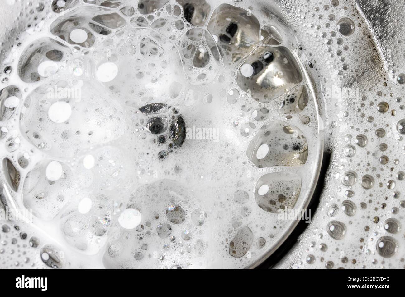 Weißer Schaum mit Reinigungsblasen in einem Waschbecken, Makroansicht.  Ablassöffnung mit Seifenblasen im Metallwaschbecken. Mechanisch  verstellbare Ablassschraube in der Nähe Stockfotografie - Alamy