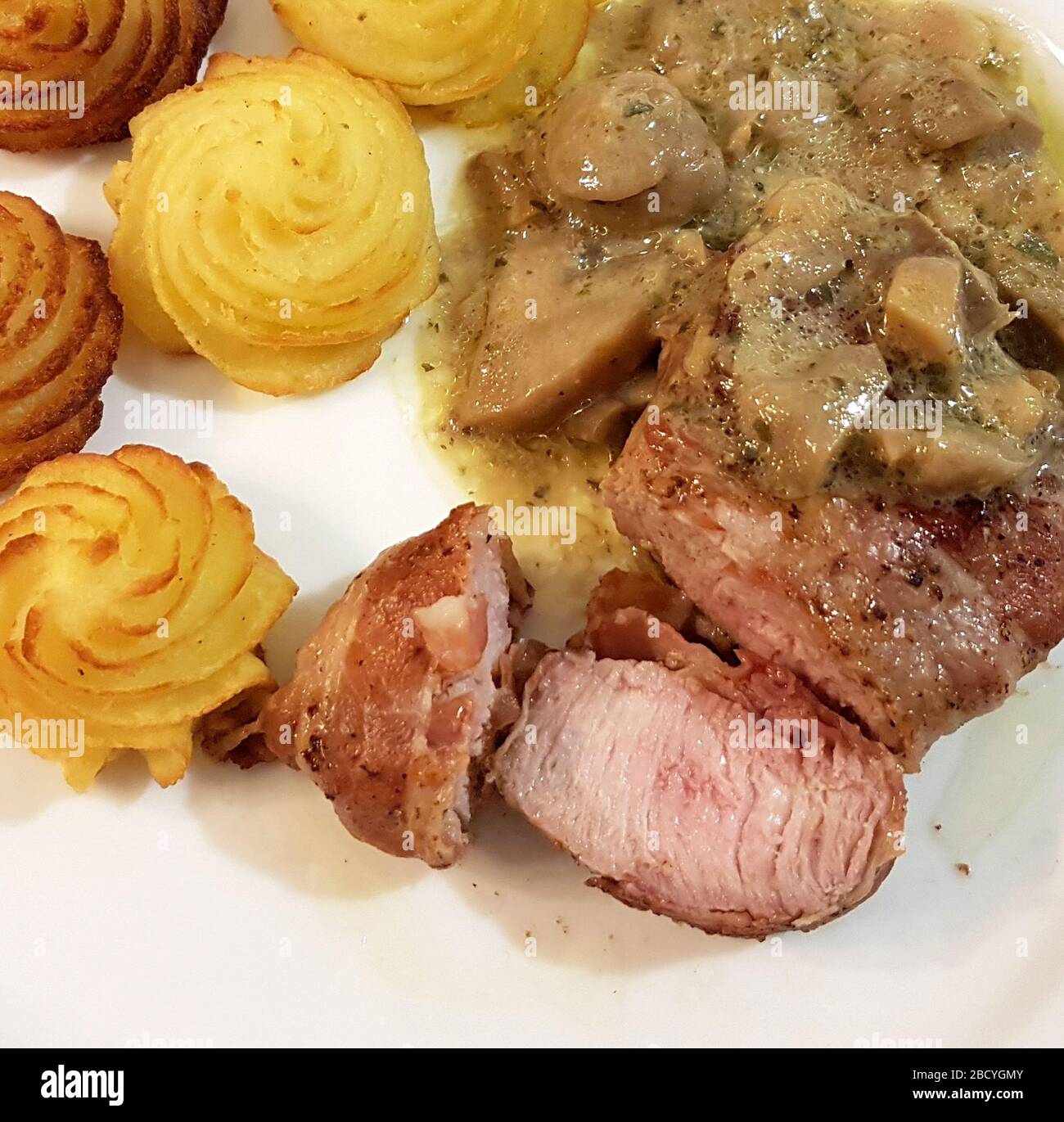 Schweinederloin in Speckkruste mit sautierten Pilzen und Herzogkartoffeln Stockfoto