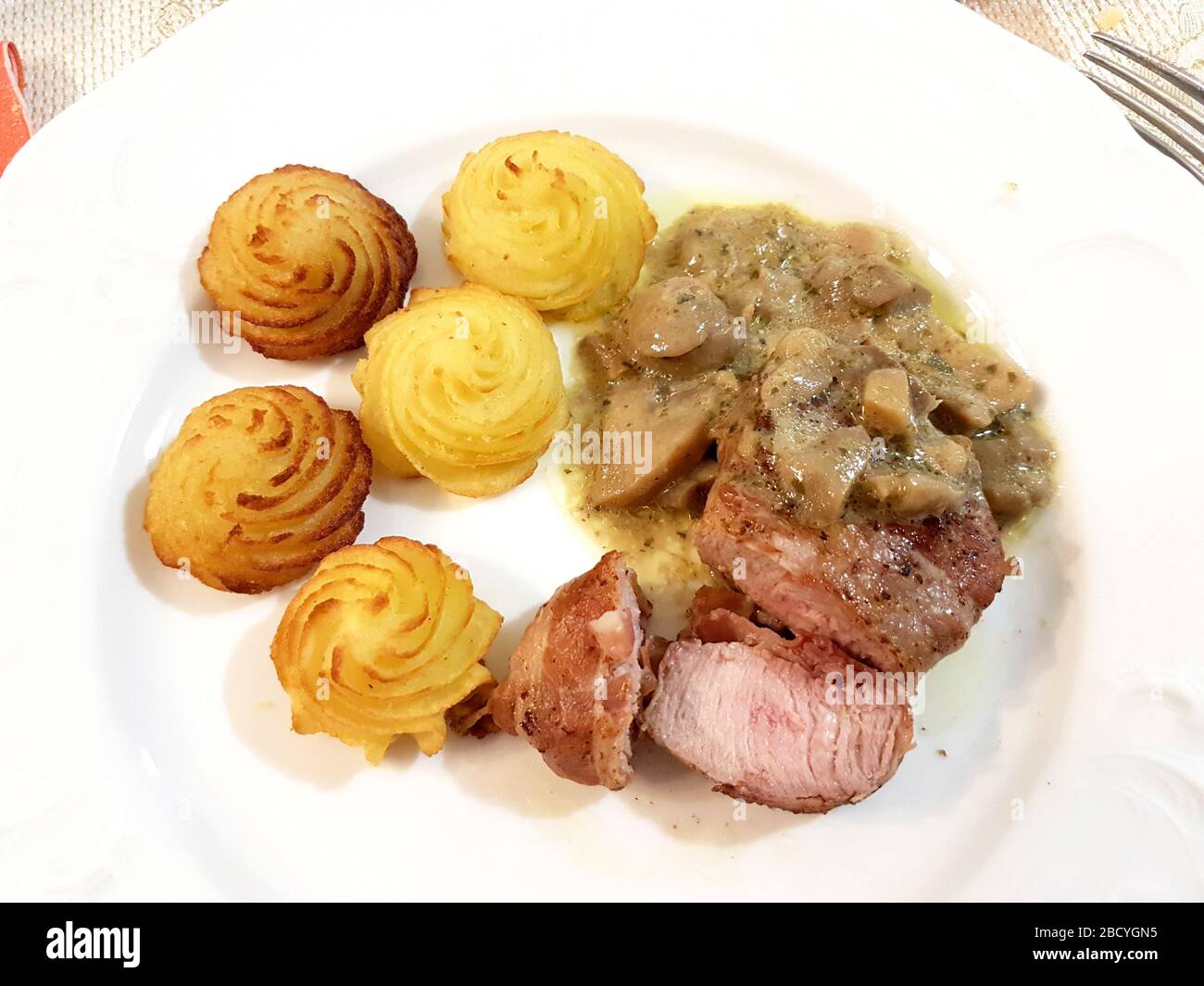 Schweinederloin in Speckkruste mit sautierten Pilzen und Herzogkartoffeln Stockfoto