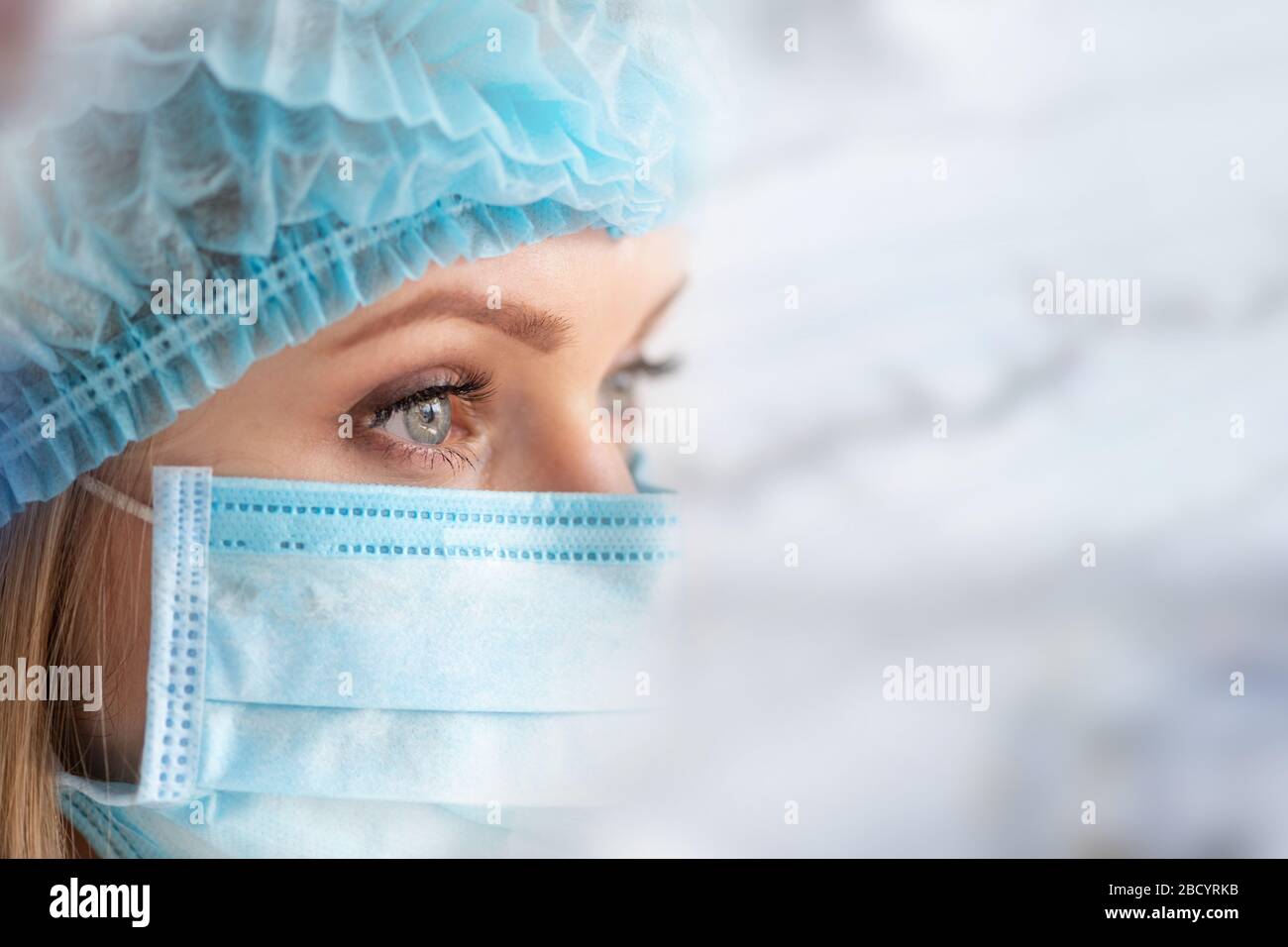 OP-Pfleger oder Arzt mit Gesichtsmaske und Kappe. Gesundheitswesen, Chirurgie. Nahaufnahme des Porträts der jungen kaukasischen Frau auf weißem Hintergrund Stockfoto